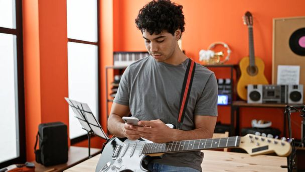 Joven músico latino usando smartphone en estudio de música - Foto, imagen