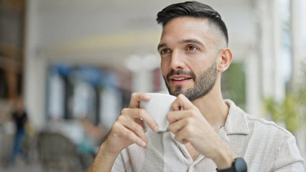 若いヒスパニックの男は,コーヒーショップテラスでコーヒーを飲む自信を持って微笑みます - 写真・画像