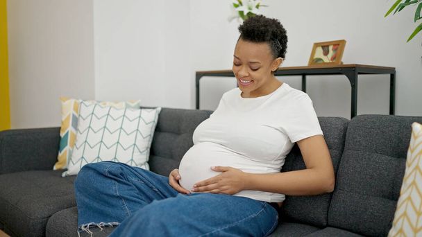 Young pregnant woman touching belly sitting on sofa at home - Foto, immagini