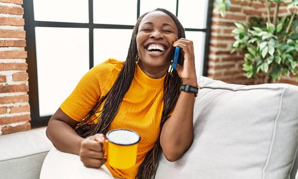 Mujer afroamericana hablando en smartphone bebiendo café en casa - Foto, Imagen
