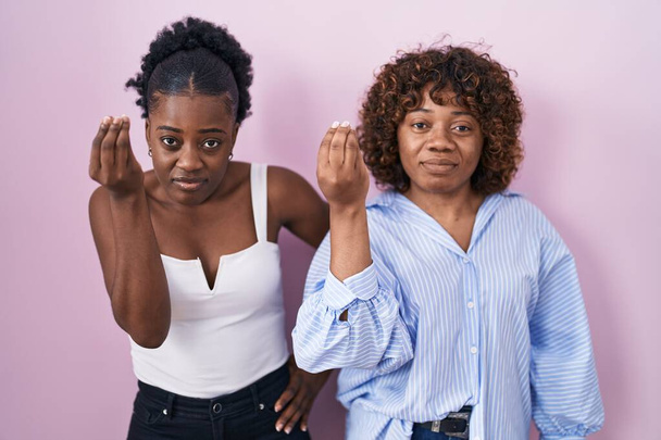 Pembe arka planda duran iki Afrikalı kadın ellerinde ve parmaklarında kendinden emin ifadeyle italyan jestleri yapıyorlar.  - Fotoğraf, Görsel