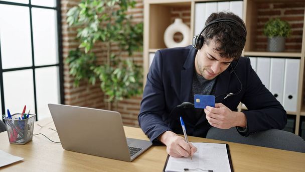 Молодий іспаномовний чоловік бізнесмен носить гарнітуру на відеовиклик за допомогою кредитної картки в офісі
 - Фото, зображення