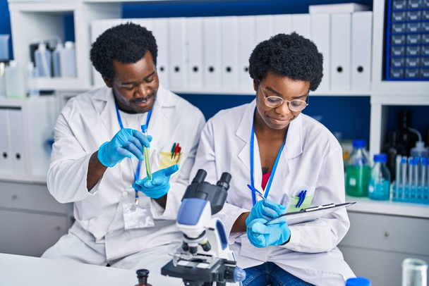 Afrikai amerikai férfi és nő tudósok írásban dokumentum tartó kémcső laboratóriumban - Fotó, kép