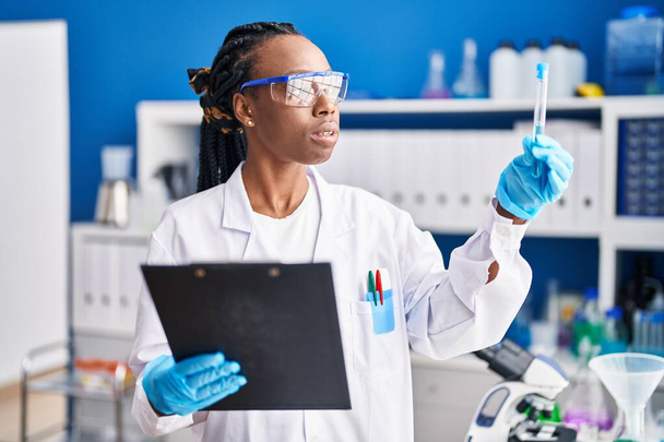 African american woman scientist holding test tube reading document at laboratory - Foto, Bild