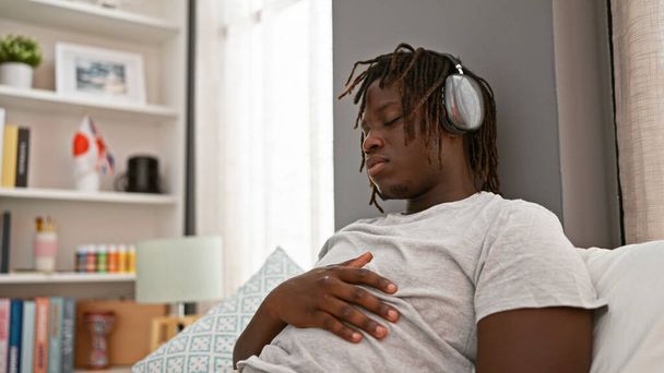 Hombre afroamericano escuchando música relajado en la cama en el dormitorio - Foto, Imagen