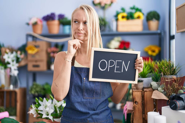 Young caucasian woman working at florist with open sign serious face thinking about question with hand on chin, thoughtful about confusing idea  - Photo, Image