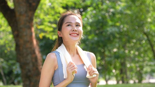 Portrait junge asiatische Frau attraktiv lächelnd und mit weißen Handtuch ruhen nach dem Training. Lächelnde, sportliche junge Frau, die draußen arbeitet und in die Kamera schaut. Gesunder Lebensstil Wohlbefinden Wellness - Foto, Bild