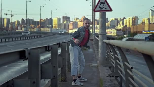 Městský chlápek tančí street dance. Most se silnicí, po které jezdí auta, a muž, který se rytmicky pohybuje v životním stylu. Vysoce kvalitní 4K záběry - Záběry, video