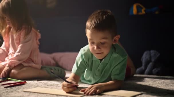 Dzieci rysują szczęśliwe dzieciństwo z ołówkami leżącymi na podłodze w domu. Piękny uśmiechnięty biały chłopiec i dziewczyna rysują i dobrze się bawią. Wysokiej jakości materiał 4k - Materiał filmowy, wideo