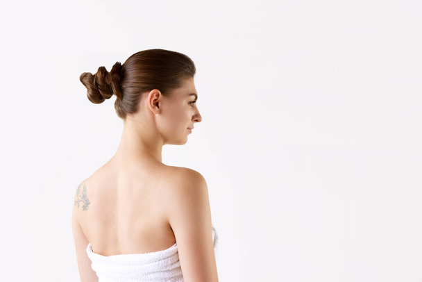 Side view image of young brunette woman standing in towel with bare shoulder after shower austin white background. Concept of female beauty, skin care, cosmetology and cosmetics, health, ad - Foto, Imagem