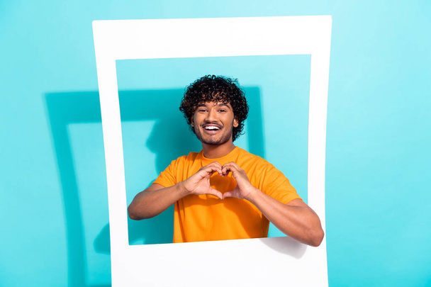 Photo of youngster guy with curly hair show heart symbol paper window zone shot valentine day postcard isolated on cyan color background. - Фото, зображення