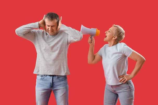 Reife Frau mit Megafon schreit ihren Mann auf rotem Hintergrund an - Foto, Bild