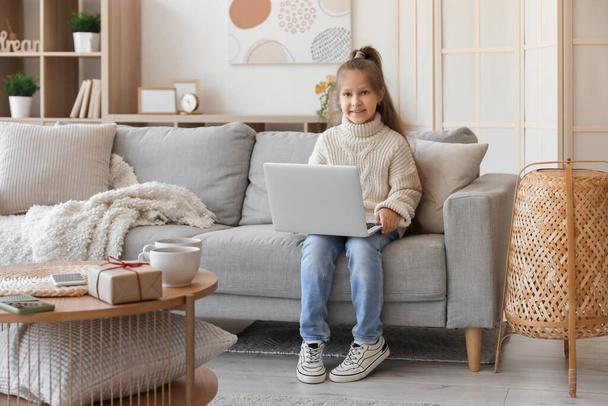 Χαριτωμένο κοριτσάκι σε πλεκτό πουλόβερ χρησιμοποιώντας φορητό υπολογιστή στο σπίτι - Φωτογραφία, εικόνα
