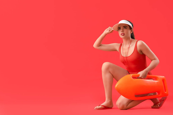 Female lifeguard with rescue buoy on red background - Photo, Image