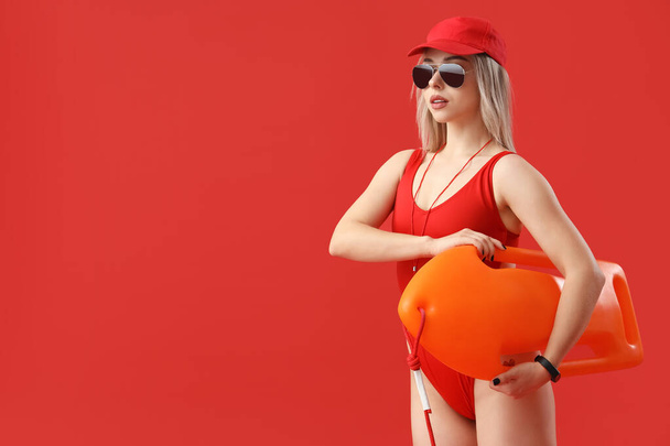 Female lifeguard with rescue buoy on red background - Photo, Image