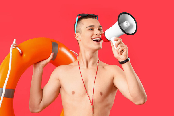 Salvavidas macho con boya de anillo gritando en megáfono sobre fondo rojo - Foto, Imagen