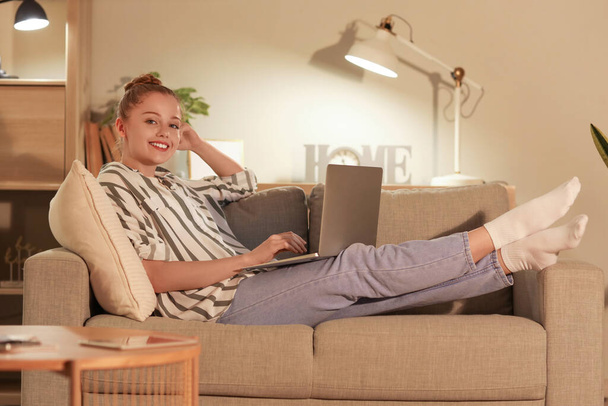 Молодая женщина работает с ноутбуком дома в вечернее время - Фото, изображение