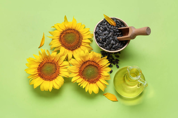 Красиві соняшники, дерев'яна миска з насінням і декантер олії на зеленому фоні - Фото, зображення
