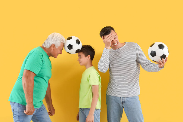 Little boy with his dad and grandfather holding soccer balls on yellow background - Photo, Image