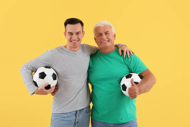Młody mężczyzna z ojcem i piłką nożną przytulający się do żółtego tła - Zdjęcie, obraz