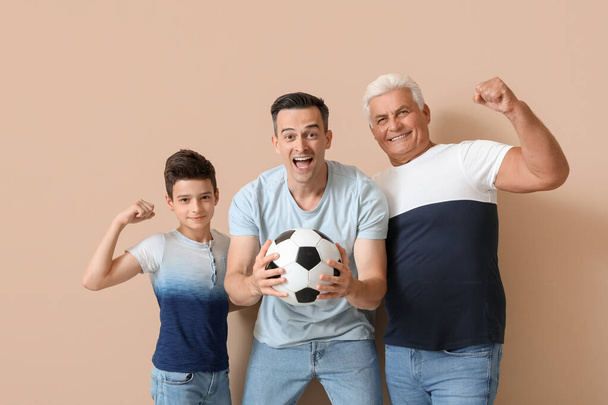 Kleine jongen met zijn vader en grootvader houden voetbal op beige achtergrond - Foto, afbeelding