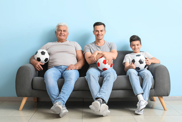 A kisfiú az apjával és a nagyapjával focimeccset néz a kék fal közelében. - Fotó, kép