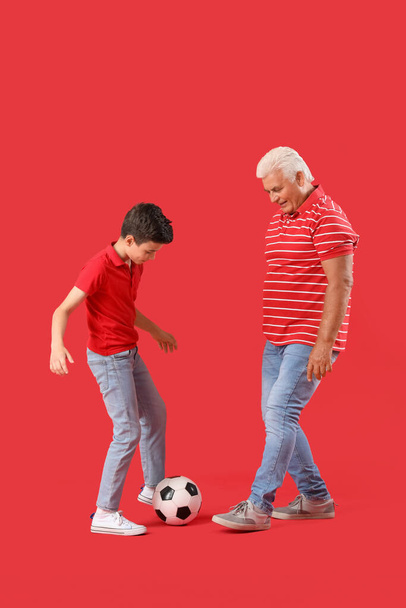 Μικρό αγόρι με τον παππού του να παίζει ποδόσφαιρο σε κόκκινο φόντο. - Φωτογραφία, εικόνα