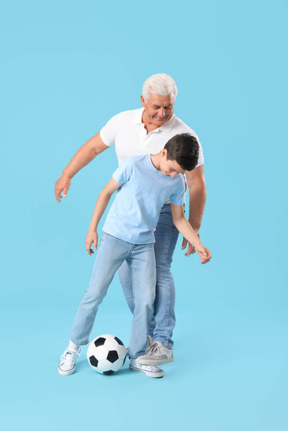 Мальчик с дедушкой играет в футбол на синем фоне - Фото, изображение