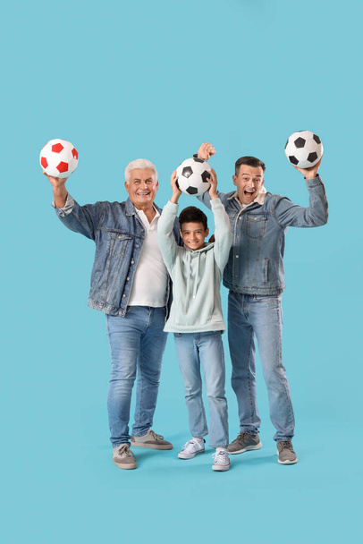 Μικρό αγόρι με τον πατέρα του και τον παππού του κρατώντας μπάλες ποδοσφαίρου σε μπλε φόντο - Φωτογραφία, εικόνα