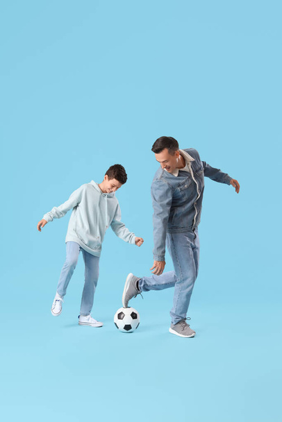 Маленький мальчик с отцом играет в футбол на синем фоне - Фото, изображение