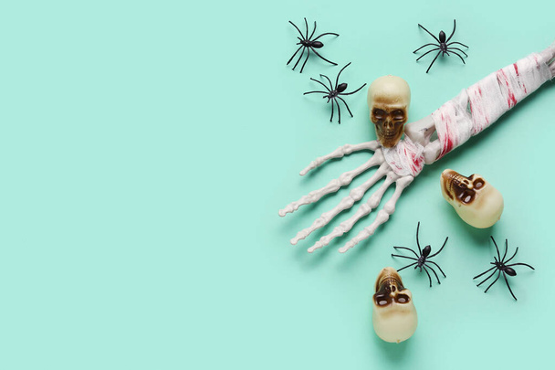 Esqueleto mano con calaveras y arañas para la celebración de Halloween sobre fondo turquesa - Foto, imagen