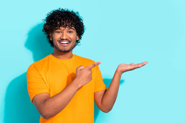 Portrait photo of young funky cheerful man curls hair wear yellow t shirt hold hand demonstrate object isolated on cyan color background. - Photo, image