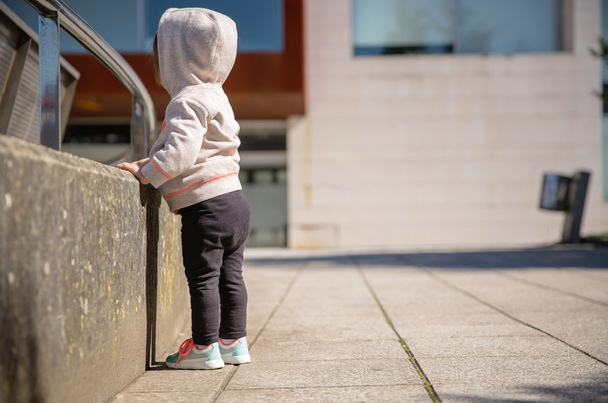 Маленькая девочка в кроссовках и толстовке стоит на улице
 - Фото, изображение