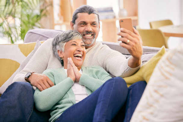 Nauraminen, selfie ja vanhempi pari, jolla on puhelin sohvalla viestintää, sosiaalista mediaa tai videopuhelua varten. Hymyile, talo ja iäkäs mies ja nainen ottavat valokuvan matkapuhelin sohvalla. - Valokuva, kuva