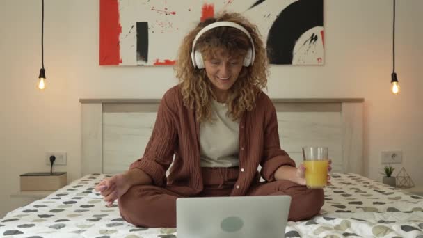 Μια καυκάσια γυναίκα με σγουρά μαλλιά κάθονται στο σπίτι χρησιμοποιούν ψηφιακή ταμπλέτα και ακουστικά για να παρακολουθήσουν ταινία ή σειρά σε απευθείας σύνδεση ρεύμα ή να έχουν κλήση βίντεο χαρούμενο χαμόγελο έχουν μια καλή στιγμή αντίγραφο χώρο - Πλάνα, βίντεο