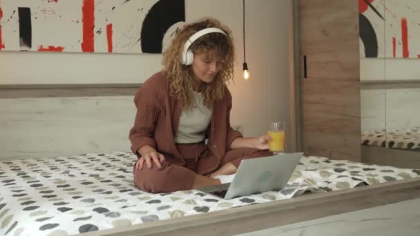 Jedna kaukaska kobieta z kręconymi włosami siedzieć w domu za pomocą tabletu cyfrowego i słuchawek do oglądania filmów lub seriali online strumienia lub mieć połączenie wideo szczęśliwy uśmiech mieć dobry czas przestrzeń kopiowania - Materiał filmowy, wideo