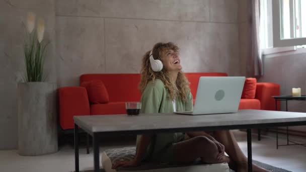 Μια καυκάσια γυναίκα με σγουρά μαλλιά κάθονται στο σπίτι χρησιμοποιούν ψηφιακή ταμπλέτα και ακουστικά για να παρακολουθήσουν ταινία ή σειρά σε απευθείας σύνδεση ρεύμα ή να έχουν κλήση βίντεο χαρούμενο χαμόγελο έχουν μια καλή στιγμή αντίγραφο χώρο - Πλάνα, βίντεο
