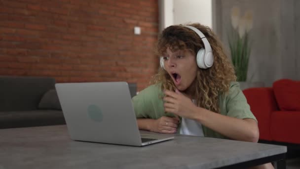 Одна біла жінка з кучерявим волоссям сидить вдома, використовує цифровий планшет та навушники для перегляду фільмів або серіалів онлайн-потоку або для відеодзвінків щаслива посмішка має гарне місце для копіювання - Кадри, відео