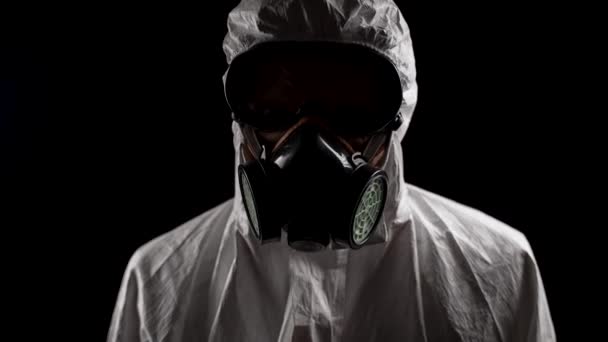 Trabajador de laboratorio en un traje de protección química jadeante levanta la cabeza sobre un fondo negro - Imágenes, Vídeo