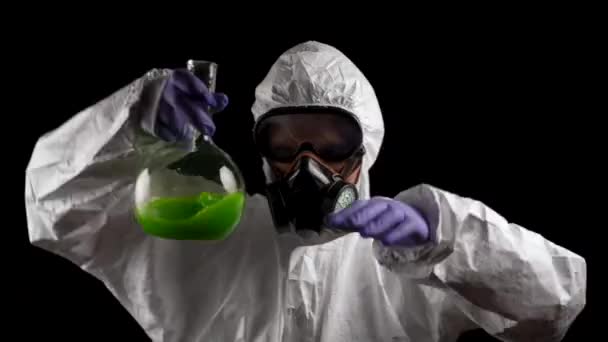 Un homme danse dans une combinaison de protection chimique avec un respirateur et des lunettes avec une solution verte dans une fiole sur un fond noir - Séquence, vidéo