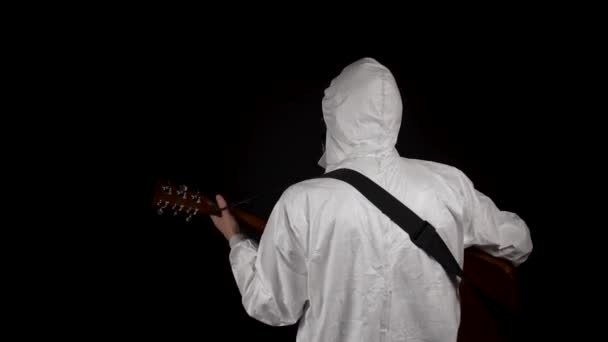 Ein Mann im Chemikalienschutzanzug mit Atemschutzmaske und Brille spielt auf schwarzem Hintergrund Gitarre - Filmmaterial, Video