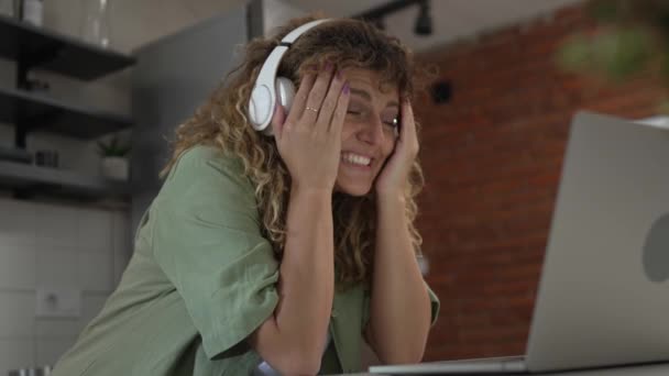 Одна біла жінка з кучерявим волоссям сидить вдома, використовує цифровий планшет та навушники для перегляду фільмів або серіалів онлайн-потоку або для відеодзвінків щаслива посмішка має гарне місце для копіювання - Кадри, відео