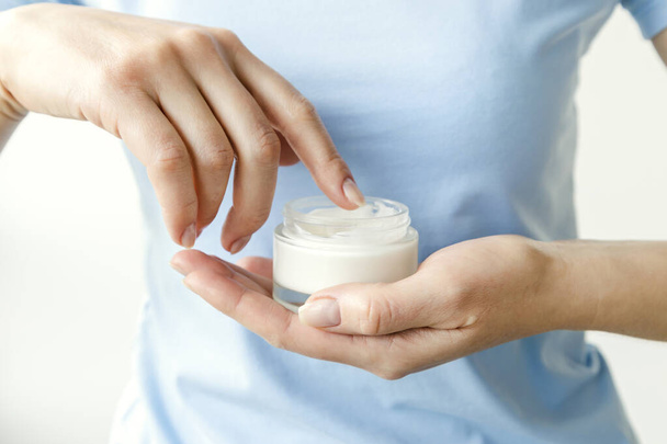 The girl takes out cosmetic cream from a glass jar with her fingers. Close up. Concept of moisturizing and skin care - Photo, Image