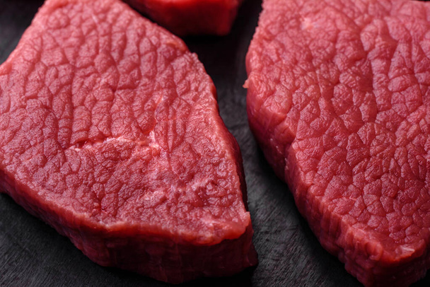 Saftiges rohes Rindfleisch mit Salz, Gewürzen und Kräutern auf dunklem Betongrund - Foto, Bild