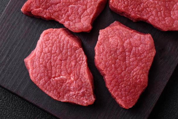 Ζουμερό νωπό κρέας βοδινού κρέατος με αλάτι, μπαχαρικά και βότανα σε σκούρο φόντο από σκυρόδεμα - Φωτογραφία, εικόνα