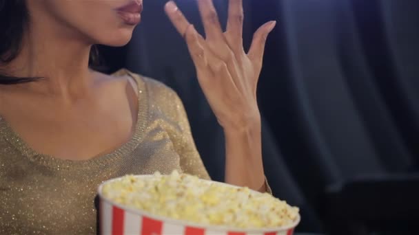 Zwarte vrouw legt haar vingers op popcorn in de bioscoop. Close-up van Afro-Amerikaanse vrouw die langzaam stukjes popcorn in haar mond stopt. Afrikaanse vrouw houdt haar vingers voor haar - Video