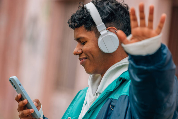 young hispanic latino man with headphones and mobile phone in the street waving - Fotó, kép