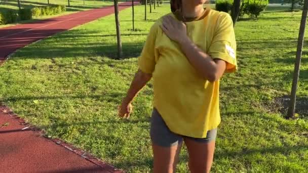 Positive multirassische junge Frau führt Morgengymnastik in ruhigen öffentlichen Park. Sie wärmt sich auf und dehnt die Schulter, indem sie bei klarem Himmel im goldenen Sonnenlicht eine Gelenkrotation macht. Aktiver Lebensstil - Filmmaterial, Video