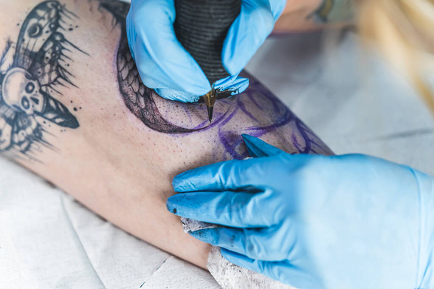 Primer plano de la máquina de tatuaje. Mujer creando imagen en la pierna con equipo de tatuaje profesional en el estudio de tatuajes. Foto de alta calidad - Foto, imagen