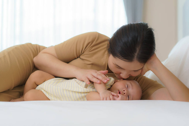 De Aziatische moeder knuffelde haar jonge zoon, zodat ze kon een goede nachtrust in de slaapkamer thuis, Vertegenwoordigt liefde en familie - Foto, afbeelding